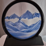 Close-up of a circular blue sand art display with a mountain landscape effect, showcasing the calming flow of sand creating mesmerizing patterns, perfect for home or office decor