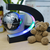 Floating globe light levitating in a C-shaped frame with a small teddy bear placed beside it on a desk, creating a cozy and decorative scene